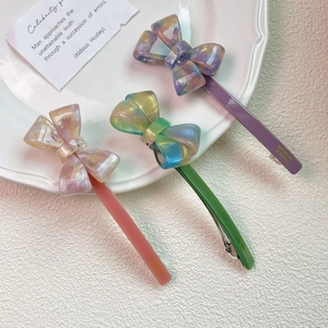 Three elegant acetate bow hair clips in pink green and purple colors on a white plate
