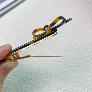 Detail of tortoiseshell bow hair clip with gold metal duckbill clamp in a hand