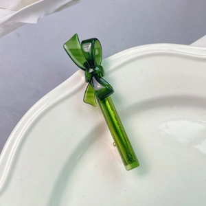 Detail of dark green acetate bow hair clip with translucent resin texture on a plate