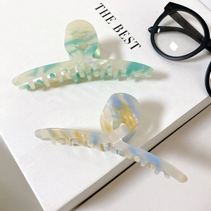 Detail of large acetate hair claws with marble texture shown on a white pedestal