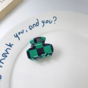 Macro detail of mini green checkered hair claw clip displayed on a white ceramic plate