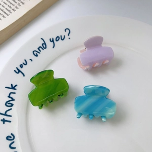Three mini acetate hair claws in purple, green and blue marble patterns on a white plate