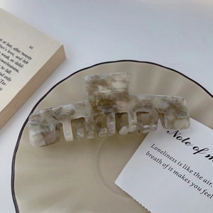 Detailed view of a marble pattern acetate hair claw clip on a minimalist ceramic plate