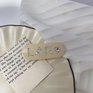 Close-up of cream acetate hair clip with sparkling rhinestone LAR letters and heart detail