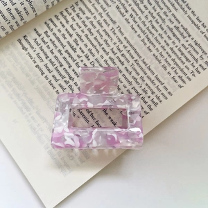 Detail of a square acetate hair claw clip with purple floral marble texture on a book