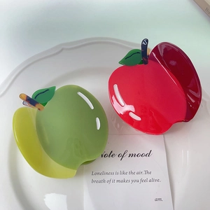 Pinces à cheveux chics en forme de pomme en acétate rouge et vert sur une assiette