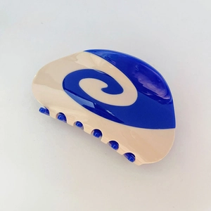 Dettaglio del fermaglio in acetato blu e crema con motivi a spirale e finitura lucida