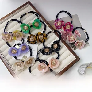 Detailed view of elegant acetate flower hair ties with rhinestones in a wooden tray