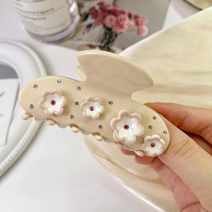 Pince à cheveux fleurie beige élégante avec strass tenue en main pour démonstration