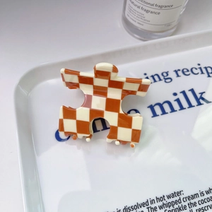 Détail d'une pince à cheveux à carreaux orange et blanc en acétate dans un plateau blanc