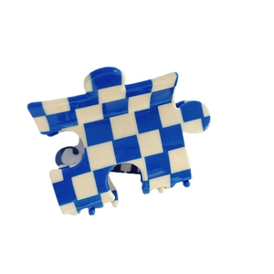 Pince à cheveux en acétate à damier bleu et blanc en forme de puzzle sur fond blanc