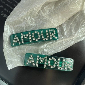 Close-up of emerald resin hair clips with rhinestone AMOUR letters on pleated paper