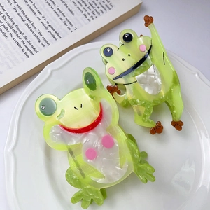 Pince à cheveux grenouille mignonne en acétate avec strass posée sur une assiette décorative