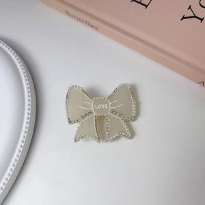 Close-up of cream bow hair clip with white pearls, rhinestones and LOVE lettering