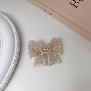 Detail of a pink marble resin bow hair clip with pearls and rhinestone Love lettering