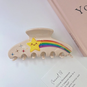 Détail d'une pince à cheveux crème avec étoile arc-en-ciel et strass colorés brillants