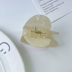 Detail of a beige heart hair claw clip with pearlescent acetate finish and gold spring