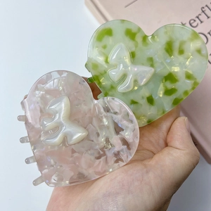 Dettaglio di fermagli per capelli a cuore in acetato rosa e verde con fiocco bianco