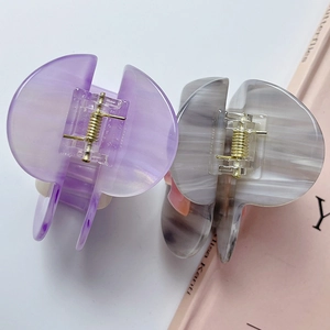 Dettaglio di grandi mollettoni per capelli in acetato con texture marmorizzate e molla oro