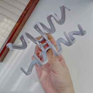 Detailed side view of a large wave-shaped light purple hair claw clip held by hand