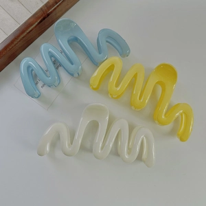 Three wave-shaped hair claws in blue, yellow, and white on a clean background