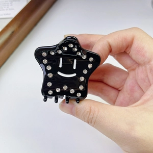 Detailed view of black star-shaped hair claw with smiling face and rhinestone edges