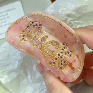 Macro detail of acetate hair claw with pink rhinestones and bold letter design