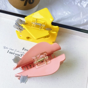 Close-up of yellow cheese hair claw and pink clip with a grey cat ornament