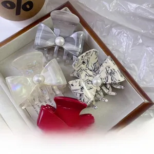 Close-up of bow-shaped acetate hair claws with inlaid pearls in four elegant colors