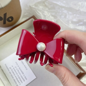 Detailed close-up of a red bow hair claw clip with a large pearl accent for women