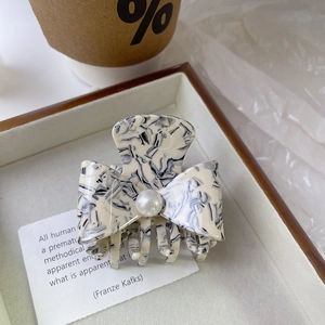 Detailed view of an elegant marble pattern bow hair claw clip with a single white pearl accent