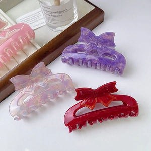 Elegant acetate bow hair claws in pink, purple, white, and red displayed on a tray