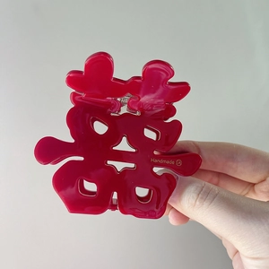 Detailed close-up of a red Chinese wedding hair claw clip with golden handmade logo