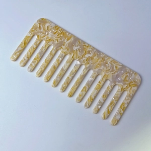 Macro view of wide-tooth acetate comb with cream yellow marble pattern texture