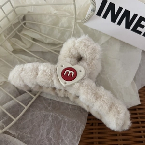 Dettaglio del fermaglio per capelli in peluche beige con cuore bianco e lettera m