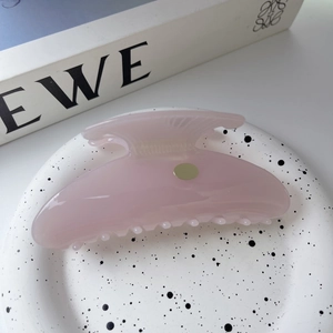 Detail of pink acetate shell hair claw clip with golden emblem on white background