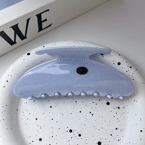 Detail of a large lilac scallop hair claw with glitter texture on a white plate
