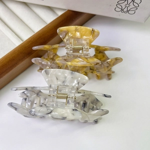 Elegant marble texture acetate claw clips in amber and white on a wooden display tray