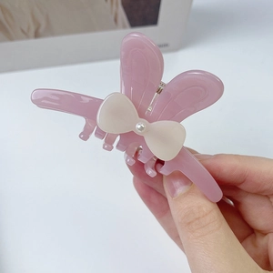 Détail de la pince à cheveux en acétate rose avec nœud dépoli blanc et perle
