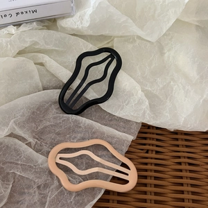 Détail de barrettes à cheveux évidées ondulées en noir et rose abricot sur tapis tissé