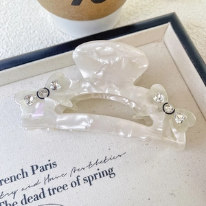 Détail de la pince à cheveux en acétate blanc avec nœud et décoration en strass étincelants