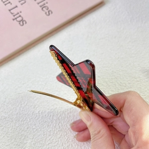 Detalle del patrón de cuadros rojos y negros en la pinza de estrella con base de metal dorado