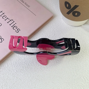 Détail d'une pince à cheveux en acétate rose et noir avec motif cœur sur un livre