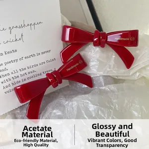 Detail of red acetate bow hair clip showing smooth texture and handmade gold lettering