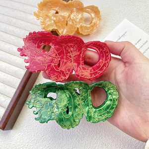 Detail of three dragon-shaped acetate hair claws in orange red and green with gold accents