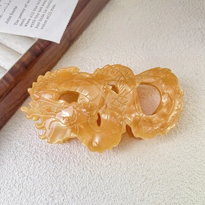Detailed close-up of amber acetate hair claw clip featuring an intricate carved dragon design