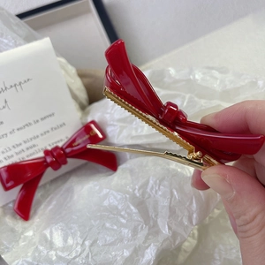 Close-up detail of a glossy red bow hair clip with golden metal duckbill clip