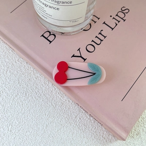 Detail view of cute pink acrylic hair clip with red cherry on a decorative book