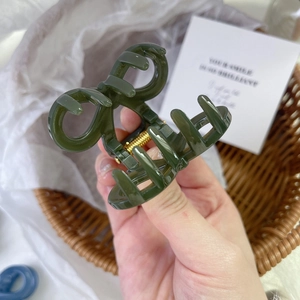 Close-up of a dark green resin bow hair claw clip with a durable gold metal spring