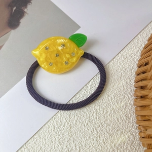 Detail of a bright yellow lemon hair tie with green leaf and small sparkling rhinestones